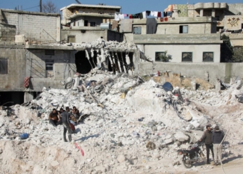 People sit on the rubble of damaged buildings in the aftermath of an earthquake, in rebel-held town of Harem, Syria February 13, 2023.  REUTERS/Mahmoud Hassano