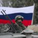 A pro-Russian man (not seen) holds a Russian flag behind an armed servicemen on top of a Russian army vehicle outside a Ukrainian border guard post in the Crimean town of Balaclava March 1, 2014. Ukraine accused Russia on Saturday of sending thousands of extra troops to Crimea and placed its military in the area on high alert as the Black Sea peninsula appeared to slip beyond Kiev's control. REUTERS/Baz Ratner (UKRAINE - Tags: MILITARY POLITICS CIVIL UNREST)